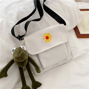 Detail of white canvas crossbody bag with sunflower embroidery and green frog plush charm