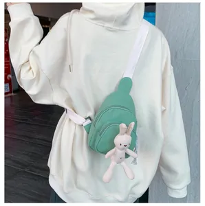 Détail du sac de poitrine en toile verte avec sangle blanche et pendentif lapin