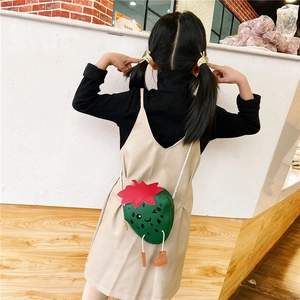 Detail view of a green strawberry-shaped kids crossbody bag with cute face and strap