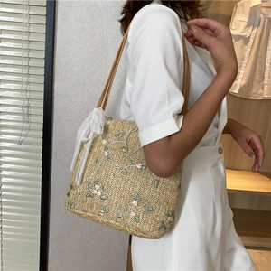 Detailed view of beige straw tote bag with floral embroidery and white lace ribbon trim