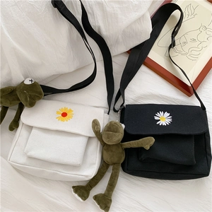 Detail of canvas crossbody bag with daisy embroidery and green frog plush keychain charm