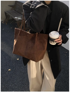 Detail of dark brown suede tote bag carried by a model in a minimalist urban setting