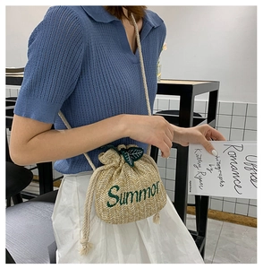 Detail of straw bucket bag featuring green 'Summer' embroidery and leaf accents