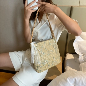 Detail of beige straw tote bag featuring floral embroidery and elegant white lace bow
