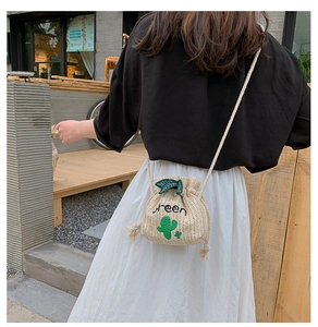 Detail of straw bucket bag with green cactus embroidery and drawstring on a model