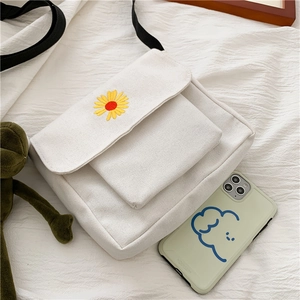 Detail view of off-white canvas crossbody bag with daisy embroidery and green accessories