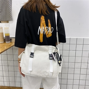 Detail of white large capacity canvas messenger bag with buckle straps and sneaker charm