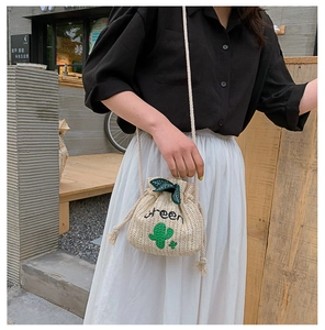 Detail of woven bucket bag featuring green cactus embroidery and leaf drawstring accents