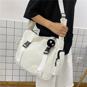 Detail of white canvas crossbody bag with black buckles and plush coal sprite charm
