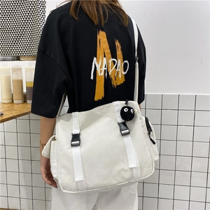 Close-up of white canvas messenger bag with double buckles and soot sprite pendant