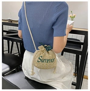 Detail of straw bucket bag with Summer embroidery and leaf drawstring on model