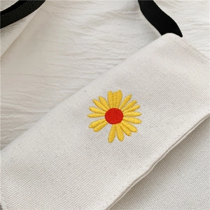 Detail of white canvas bag with yellow daisy embroidery and black fabric strap