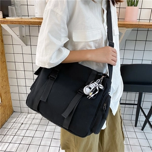 Detail of black canvas messenger bag featuring buckle straps and a mini shoe charm