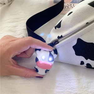 Close-up of a glowing LED cow keychain pendant with a cow-patterned canvas bag