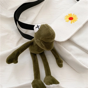 Detail of white canvas crossbody bag featuring sunflower embroidery and a plush frog charm