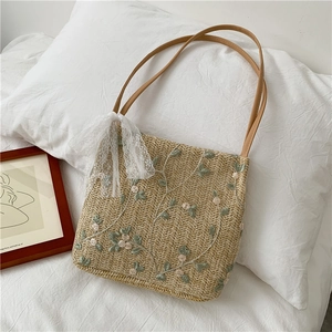 Detail of straw shoulder bag with floral embroidery and white lace bow decoration