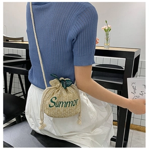 Detail of straw bucket bag featuring Summer embroidery and leaf charms on cotton rope strap