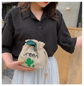 Detail of woven straw bucket bag with cactus embroidery and green leaf drawstring detail