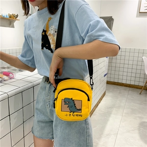Détail du sac bandoulière en toile jaune avec un dinosaure de dessin animé et texte