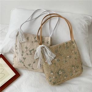 Detail of straw shoulder bags with floral embroidery and white lace bow accents