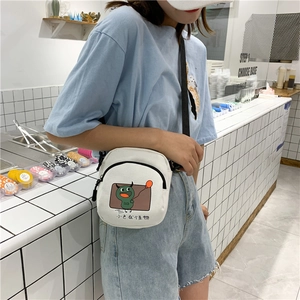 Détail du sac bandoulière en toile blanche avec petit monstre vert et sangle