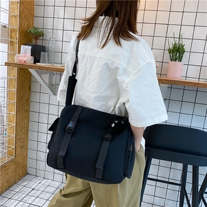 Close-up of black canvas messenger bag with flap buckles and side zipper pockets