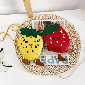 Flat lay of strawberry-shaped kids' PU leather crossbody bags on a woven mat