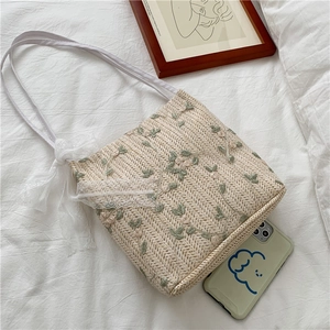 Detail of straw tote with green floral embroidery and white lace bow and phone for size