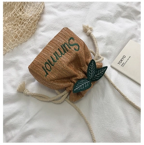 Detail of straw bucket bag with Summer embroidery and green leaf accents on white fabric
