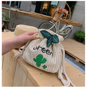Detail of straw woven bucket bag with cactus embroidery and green leaf drawstring
