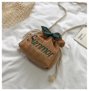 Macro detail of hand-woven straw bucket bag with green Summer embroidery and leaf charms