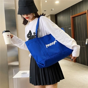 Detail of royal blue canvas tote bag with NNNVA white lettering shown on shoulder