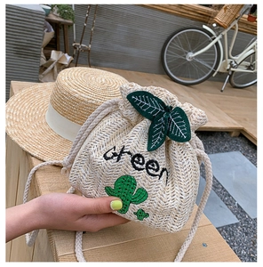 Close-up of straw bucket bag with cactus embroidery and green leaf drawstring detail