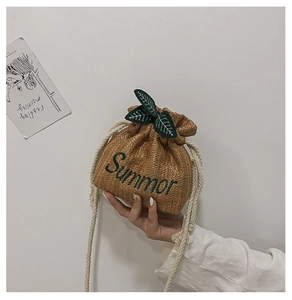Detail of woven straw bucket bag with green leaf accents and Summor embroidery
