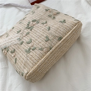 Detail of woven straw bag with floral embroidery and delicate white lace trim accents