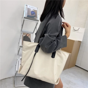 Detail of a large cream tote bag with black contrast handles shown on shoulder