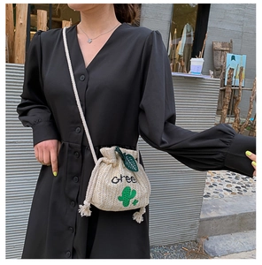 Detail of straw drawstring bucket bag featuring green cactus embroidery and shoulder strap
