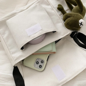 White canvas crossbody bag with compartments and green frog charm accessory
