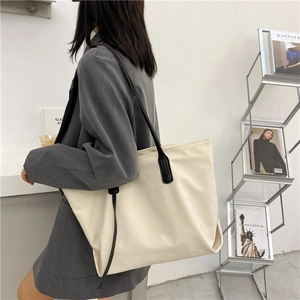 Detail of beige large capacity tote bag with black straps worn with a grey blazer