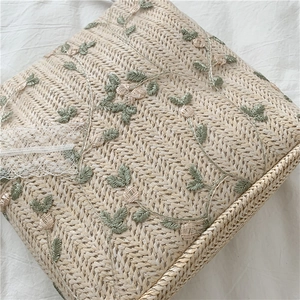 Detailed close-up of straw woven bag with white lace ribbon and green floral embroidery