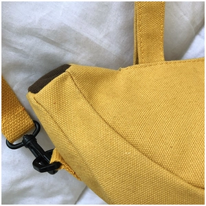 Détail du sac en toile jaune montrant la texture du tissu et les boucles en métal noir