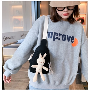 Détail d'une peluche lapin sur un sac bandoulière en toile noire avec large sangle blanche
