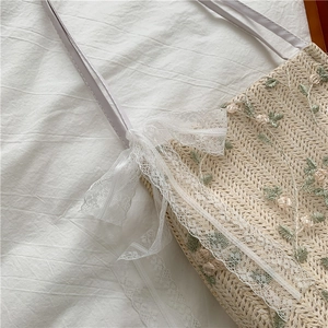 Close-up of straw tote bag featuring floral embroidery, lace trim, and a delicate bow detail