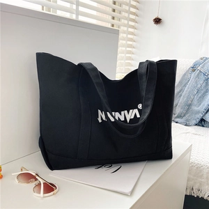 Detail of black canvas tote bag with NANNYA lettering and stylish lifestyle props