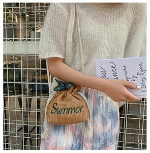 Detail of hand-woven straw bucket bag with green leaf charm and Summor embroidery
