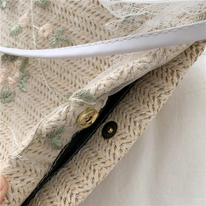 Macro view of lace overlay on straw bag with floral embroidery and gold magnetic buckle