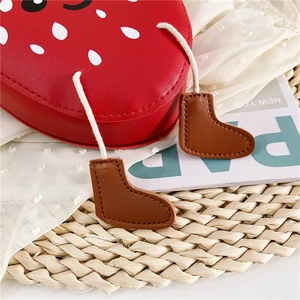 Detail of red strawberry girls crossbody bag with cute boots pendants and leather texture