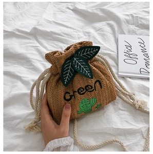 Detail of straw bucket bag featuring green leaf appliques and rustic rope shoulder strap