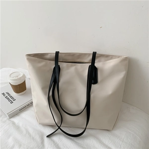 Close-up of a minimalist cream-colored tote bag with black handles in an urban setting
