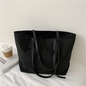Detail view of a large black tote bag on a white table with a coffee cup and books
